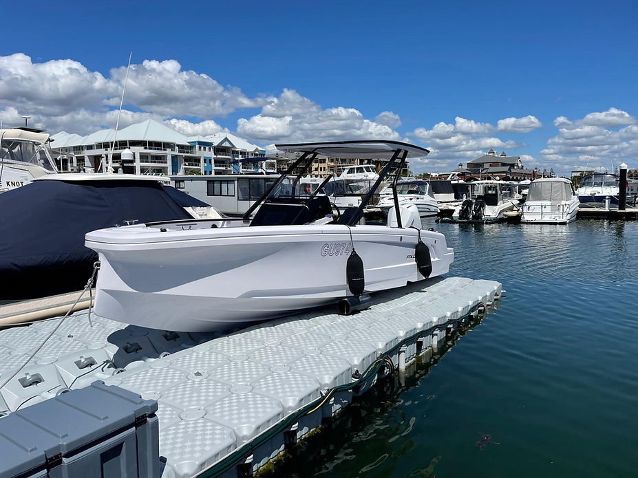 A boat is securely docked at a floating dock within a marina, surrounded by calm waters and other vessels.