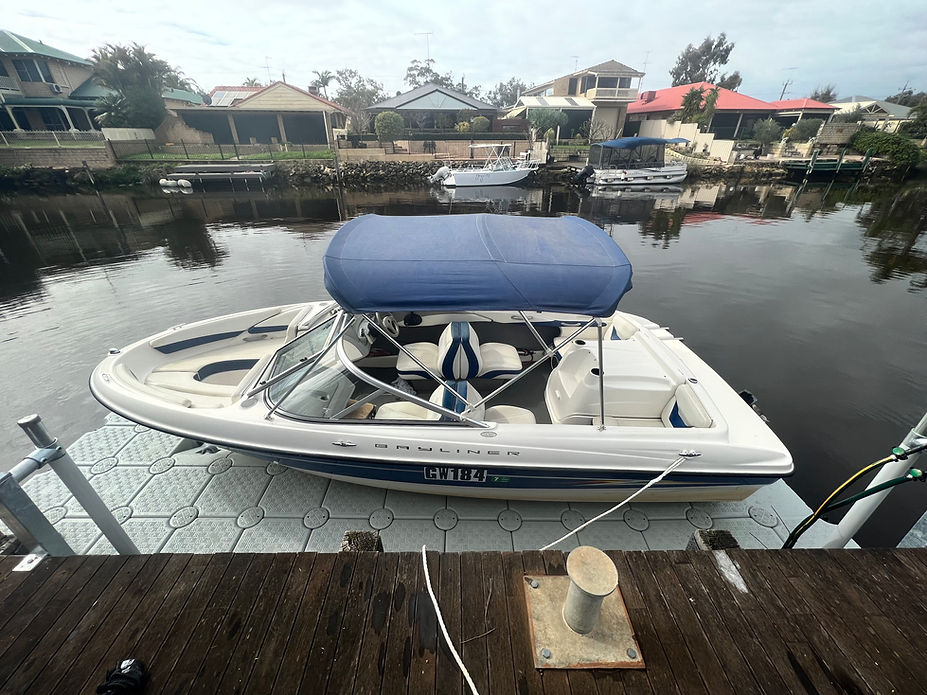 A boat with a blue canopy rests on a floating dock, surrounded by calm waters and a clear sky.