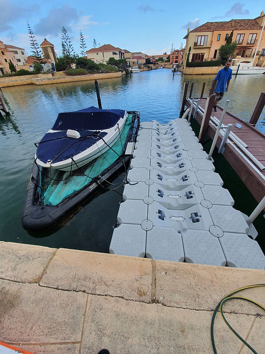 A boat securely tied to a floating dock, gently swaying in the water under a clear blue sky.